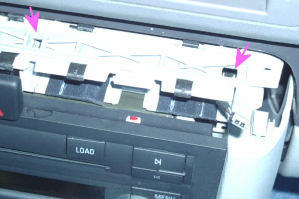 Holes where small screwdriver or radio removal tools are inserted to depress tabs on the Audi A4 cup holder module.